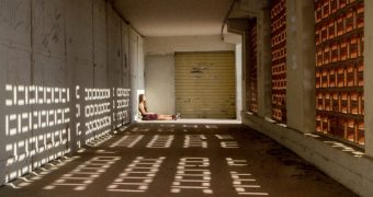 une femme assise au sol dos au mur et jambe allongées, vue de côté, la lumière sur elle