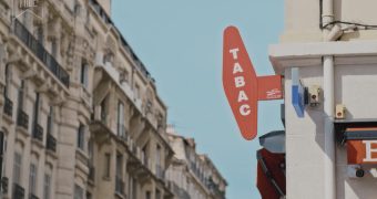 une enseigne de bar tabac vue depuis la rue avec un ciel bleu et un immeuble haussmanien en fond