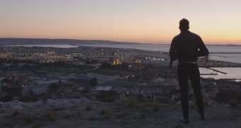 un homme de dos au soleil couchant sur une colline surplombant un aéroport au bord de mer